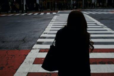 A woman stands on a city crosswalk, hesitant about walking towards a crowded sidewalk, highlighting the detachment of schizoid personality disorder.